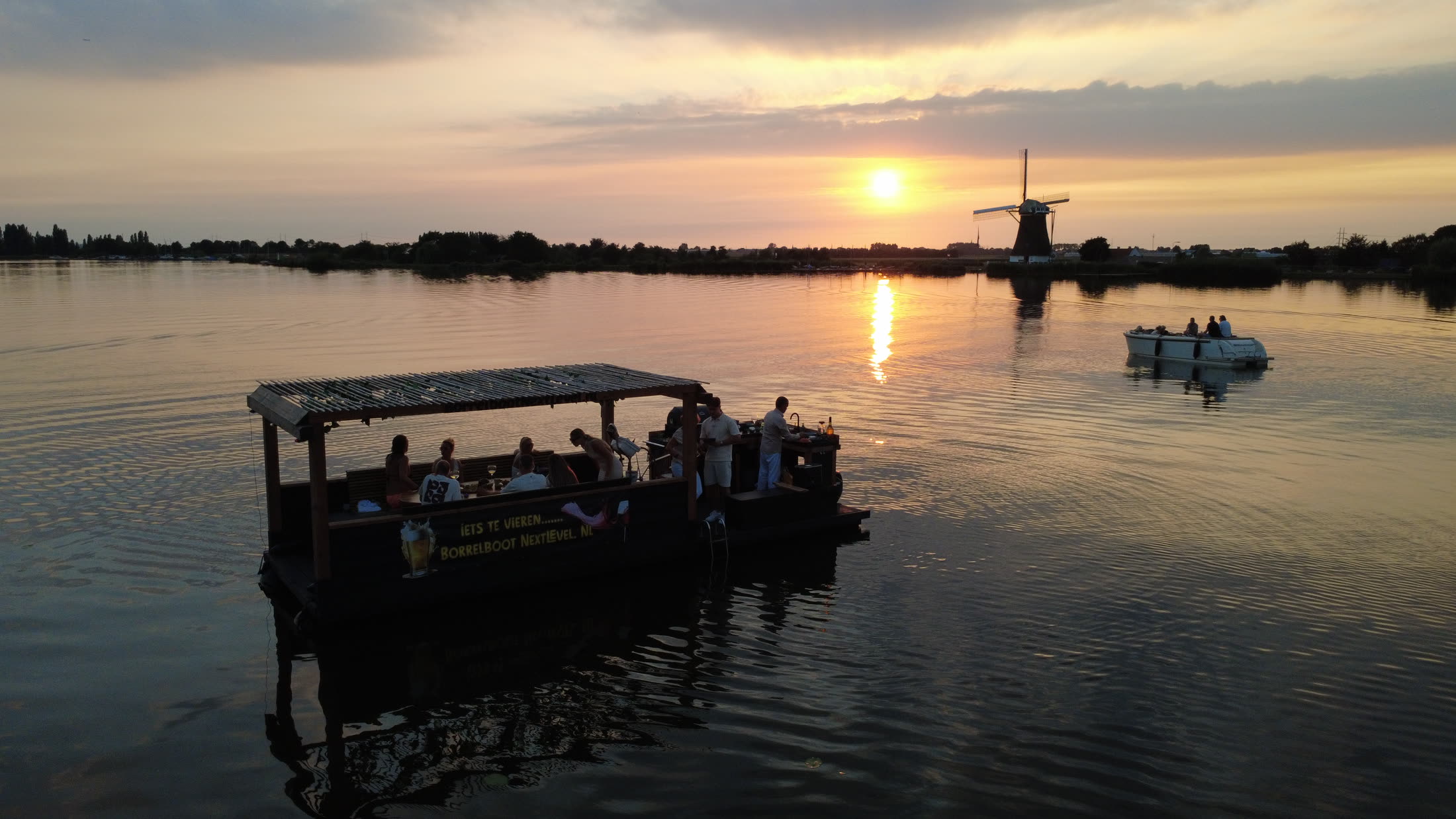 Borrelboot Nextlevel varend bij zonsondergang met een molen in beeld